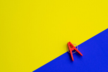 Plastic clothes pin red color, isolated on yellow blue background.