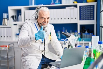 Middle age man with grey hair working at scientist laboratory doing video call smiling happy and positive, thumb up doing excellent and approval sign