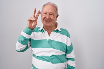 Senior man with grey hair standing over white background smiling looking to the camera showing fingers doing victory sign. number two.