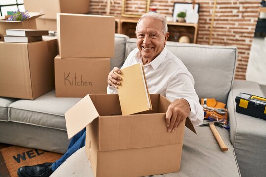 Senior man smiling confident unboxing package at new home