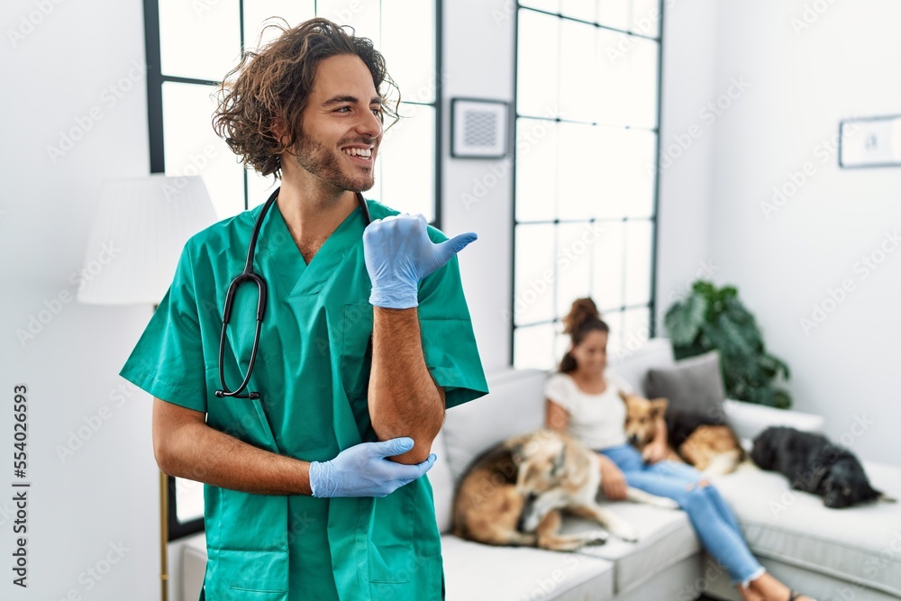 Sticker young veterinarian man checking dogs at home smiling with happy face looking and pointing to the sid