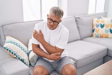 Fototapeta premium Middle age grey-haired man sitting on sofa suffering for elbow pain at home