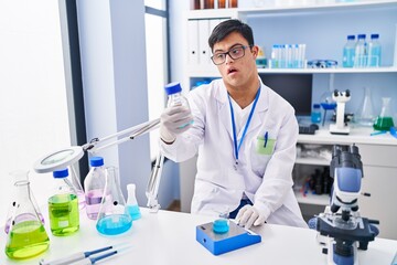 Down syndrome man wearing scientist uniform measuring liquid at laboratory