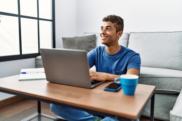 Young hispanic man using laptop sitting on the floor at home