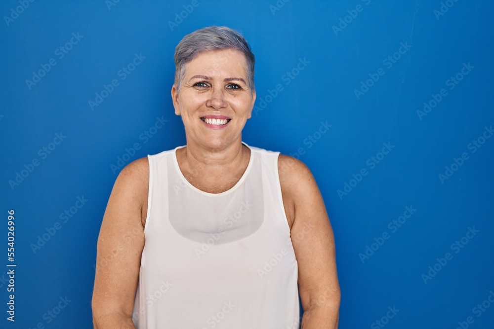 Sticker middle age caucasian woman standing over blue background relaxed with serious expression on face. si