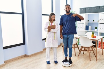 Fototapeta premium Dietitian at the clinic with client checking weight pointing finger to one self smiling happy and proud