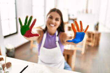 Young beautiful hispanic woman artist showing painted hands at art studio