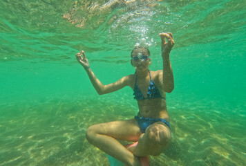 Teenager girl have fun on summer vacation doing yoga pose underwater.