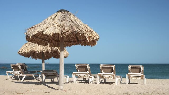 Straw umbrellas on the beach with no people at dawn and row of empty sun loungers. Vacation on the seashore with a beautiful landscape