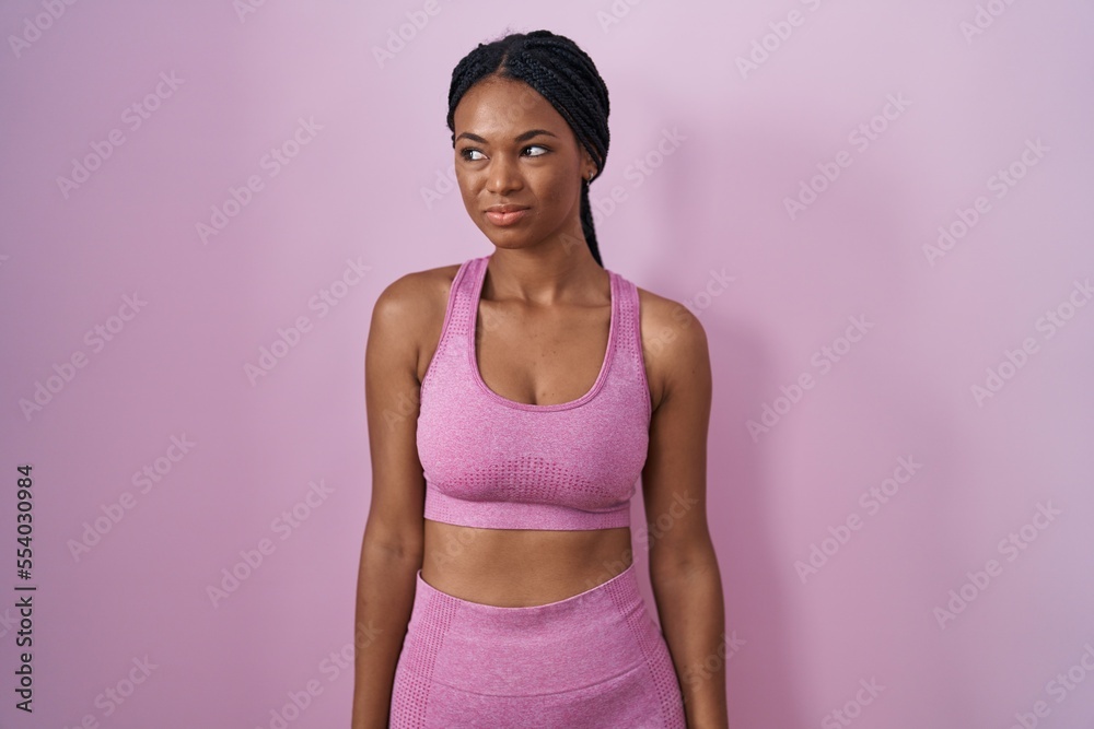 Sticker african american woman with braids wearing sportswear over pink background smiling looking to the si