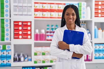 African american woman pharmacist smiling confident holding clipboard at pharmacy