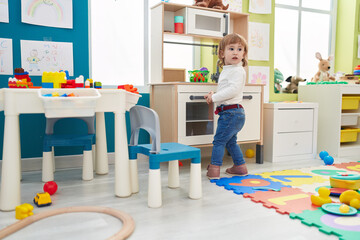 Adorable hispanic girl playing with play kitchen standing at kindergarten