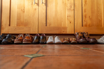 Row of shoes on a tiled kitchen floor with cupboards in the background
