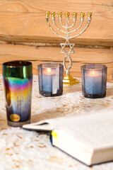 Burning candles on the table next to the siddur and menorah.