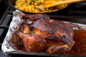 Whole chicken baked in sauce on foil in the background a frying pan with pasta.