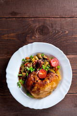 Pasta with vegetables and baked chicken leg with tomatoes sprinkled with green onions in a plate on a wooden table.copy space