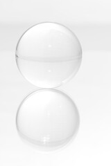 Glass ball on a mirrored surface and white background.