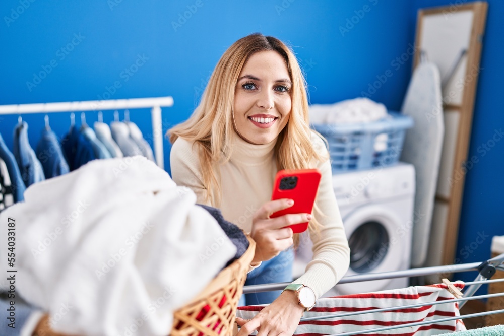 Sticker Young blonde woman using smartphone hanging clothes on clothesline at laundry room - Stickers