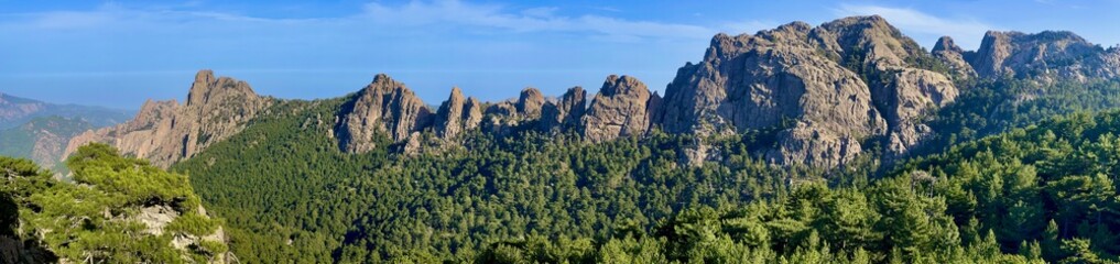 Very rocky Corsican mountain range of the Aiguilles de Bavella in summer, very tall and wide massif of France, near Zonza in Conca forest, with some trees in bottom