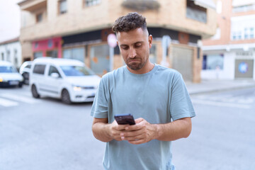 Young hispanic man using smartphone with serious expression at street