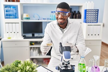 Young african american man wearing scientist uniform using microscope at laboratory