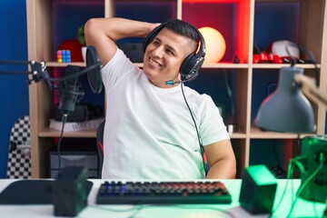 Young hispanic man playing video games smiling confident touching hair with hand up gesture, posing attractive and fashionable