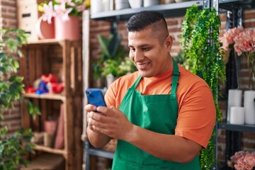Young latin man florist smiling confident using smartphone at flower shop