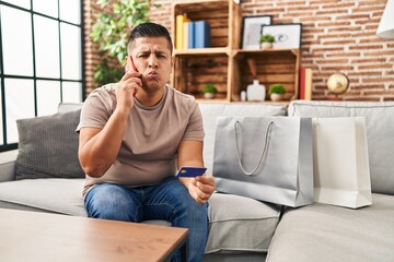 Hispanic young man doing payment with credit card on the phone looking at the camera blowing a kiss being lovely and sexy. love expression.