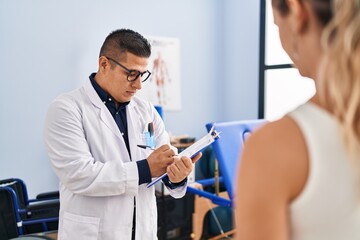 Obraz premium Young latin man pysiotherapist writing on report speaking with patient at rehab clinic