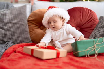 Adorable toddler wearing christmas hat sitting on sofa with present at home