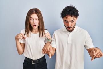 Young couple wearing casual clothes standing together pointing down with fingers showing advertisement, surprised face and open mouth
