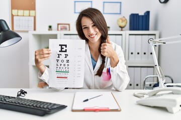 Obraz na płótnie Canvas Young doctor woman holding eyesight test smiling happy and positive, thumb up doing excellent and approval sign