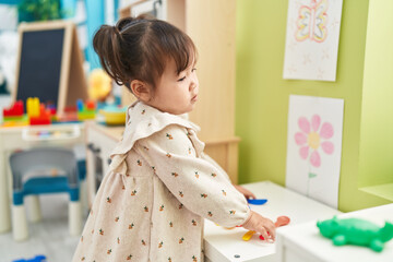 Adorable chinese girl holding cookware toy standing with relaxed expression at kindergarten