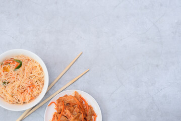 Delicious asian funchose salad and soy vegan meat salad in white bowls with wood sticks on grey background. Selective focus. Asian food concept