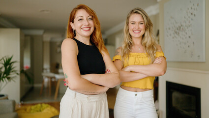 Two women smiling confident standing with arms crossed gesture at home
