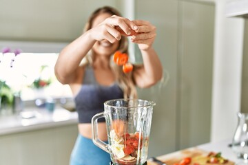 Young woman smiling confident pouring strawberries on blender at kitchen
