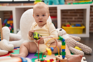 Adorable caucasian baby playing with car toy sitting on floor at kindergarten