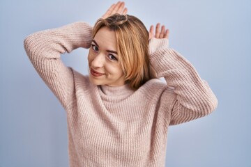 Hispanic woman standing over blue background doing bunny ears gesture with hands palms looking...