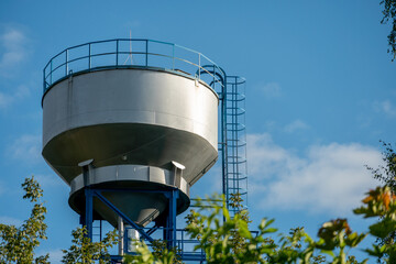 New modern water tower on the background of blue sky and forest. Methods of water storage for irrigation of agricultural crops in difficult climatic and weather conditions. A barrel with water