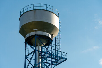 New modern water tower on the background of blue sky and forest. Methods of water storage for irrigation of agricultural crops in difficult climatic and weather conditions. A barrel with water