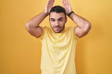 Fototapeta na wymiar Young hispanic man standing over yellow background doing bunny ears gesture with hands palms looking cynical and skeptical. easter rabbit concept.