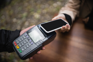 Cropped view of waiter holding payment terminal near customer with smartphone in outdoor cafe.