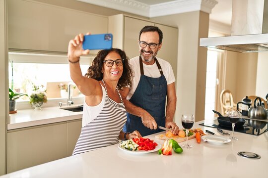 Middle age hispanic couple smiling confident cooking and make selfie by the smartphone at kitchen