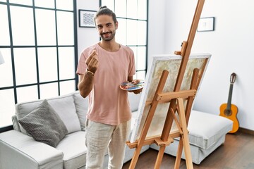 Young hispanic man with beard painting on canvas at home doing money gesture with hands, asking for...