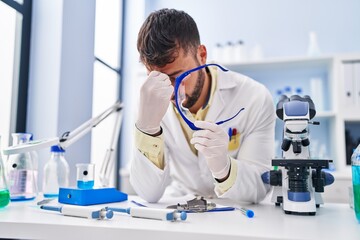 Fototapeta premium Young hispanic man wearing scientist uniform stressed working at laboratory