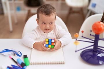Adorable toddler playing with rubik cube sitting on table at kindergarten