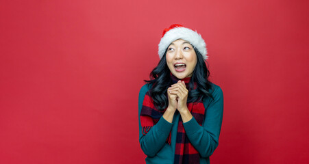 Pretty smiling asian woman in warm christmas sweater and santa hat is having excitement on red background for season celebration concept with copy space 