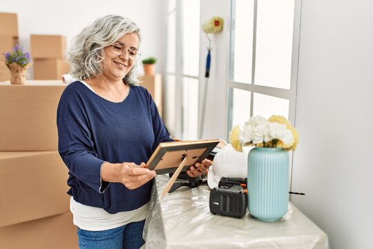 Middle age grey-haired woman smiling happy holding picture at new home.