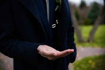 Groom holding wedding rings in hand. Two wedding rings on the floor with contrast wedding rings on floor, on ground, on piano, in hand