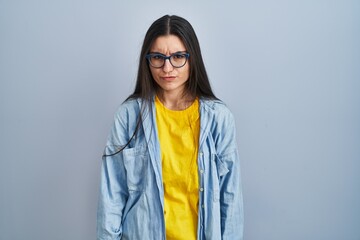Young hispanic woman standing over blue background skeptic and nervous, frowning upset because of...
